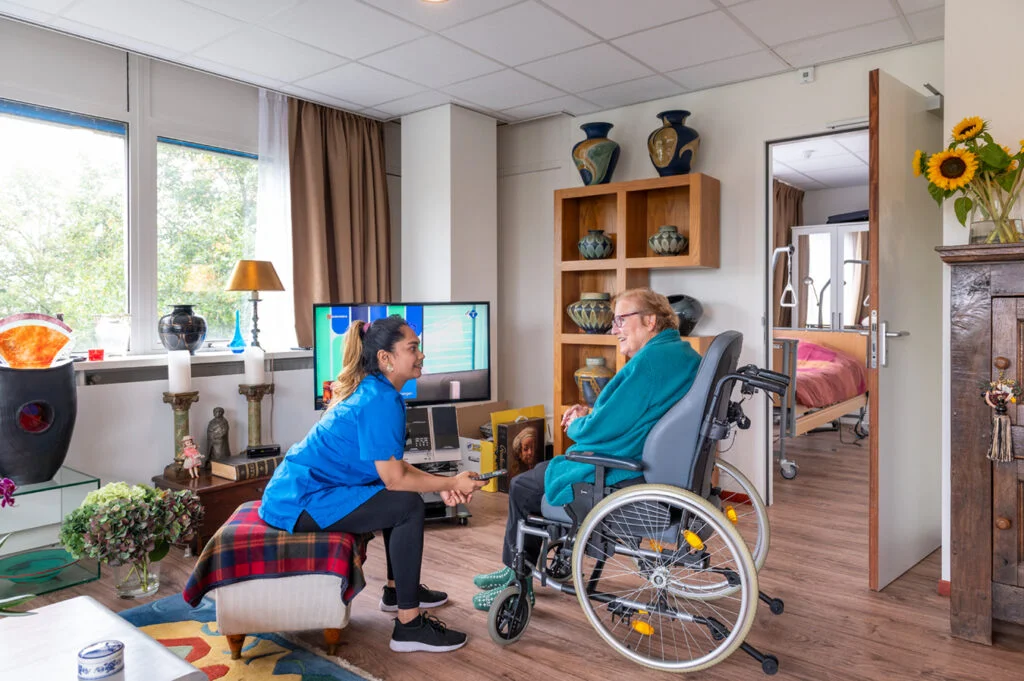 Zorgmedewerker en bewoner in een woonzorgappartement met tv en zorgvoorzieningen