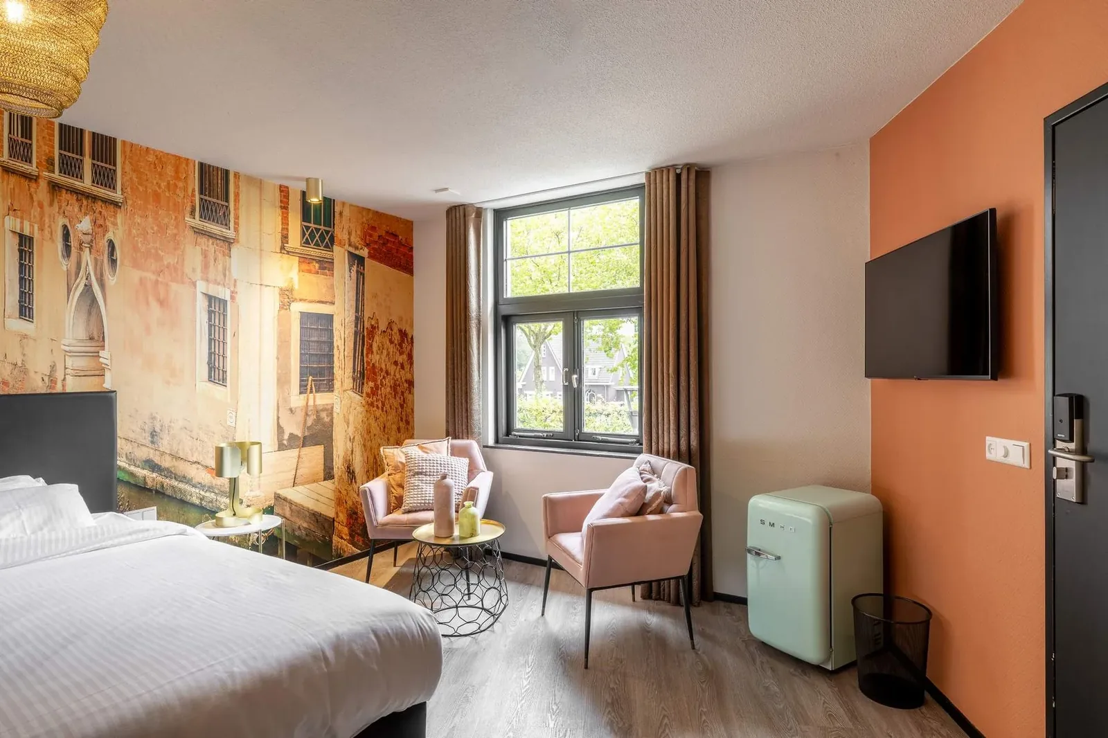 Hotelkamer van Boutique Hotel de Statie met groot bed, roze fauteuils en wandgemonteerde IPTV-televisie