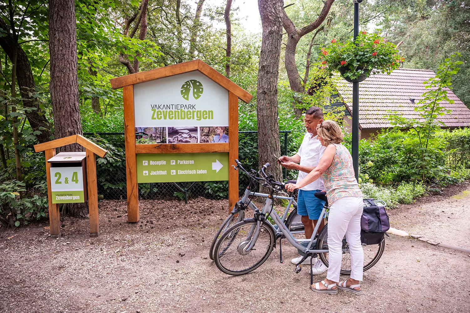 Twee fietsers bij een houten informatiebord op het beboste terrein van Vakantiepark Zevenbergen